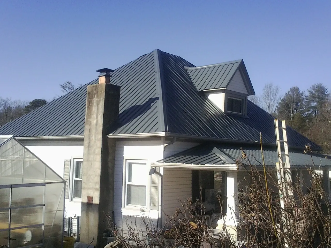 Dark blue standing seam metal roof on a white farmhouse with dormer — Slate & Tile Roof Repair by Roofing Brothers in Cibolo