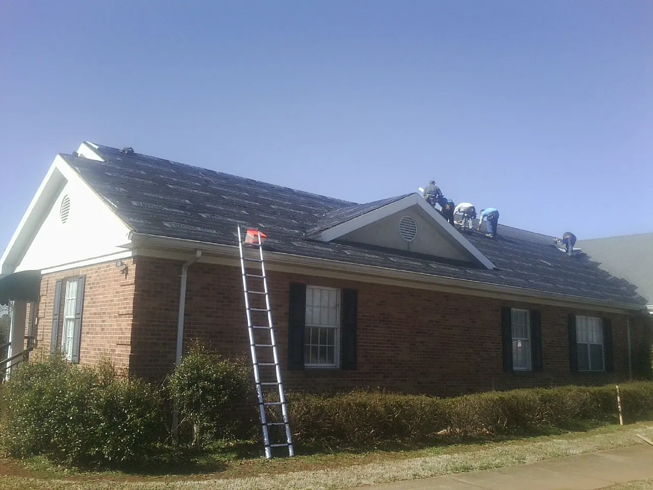 Crew tearing shingles off a brick ranch roof with a ladder set — Metal Roof Repair work by our crew in Cibolo