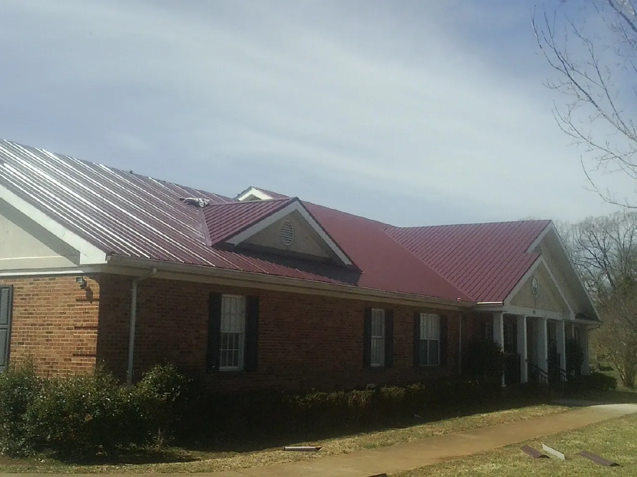 Red metal roof with gabled entries on a long brick building, from a Hail Damage Roof Repair job in Cibolo