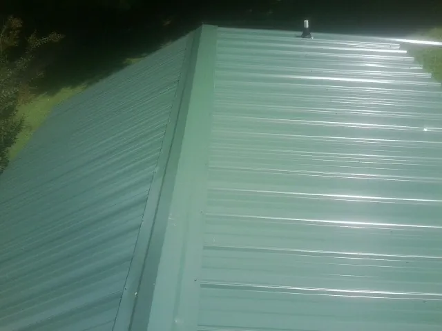 New green metal panels meeting at the ridge of a roof — Flat Roof Repair work by our crew in Cibolo