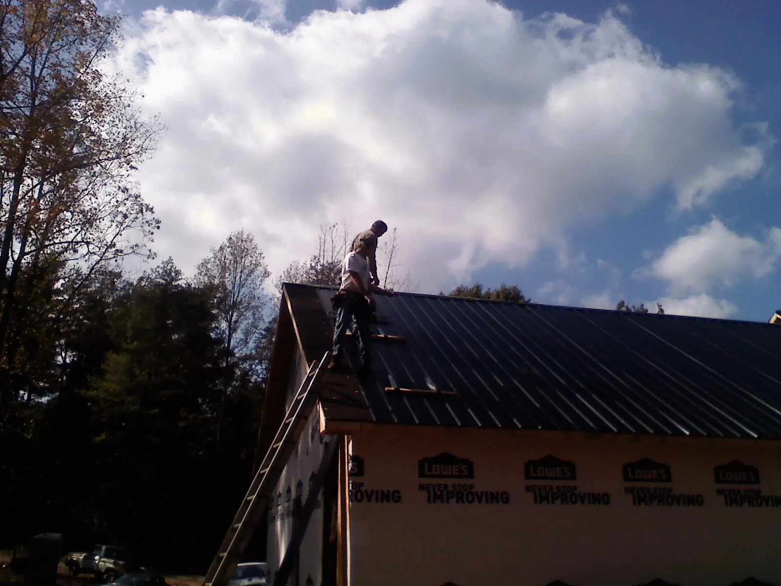 Roofer fastening dark metal panels high against a cloudy sky, from a Roof Inspection job in Cibolo